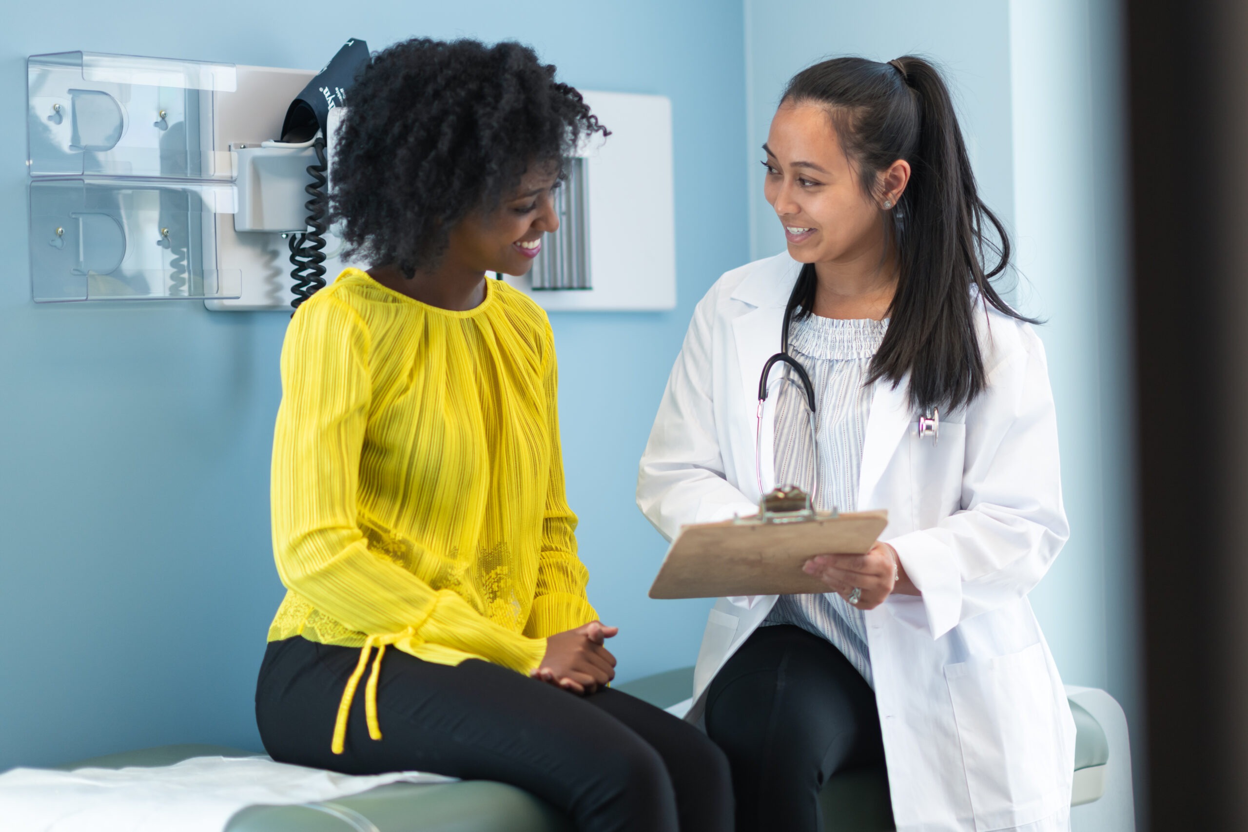 Young woman in a yellow top talking with a female MOGA physician during a gynecology visit at an OB/GYN in Memphis, TN